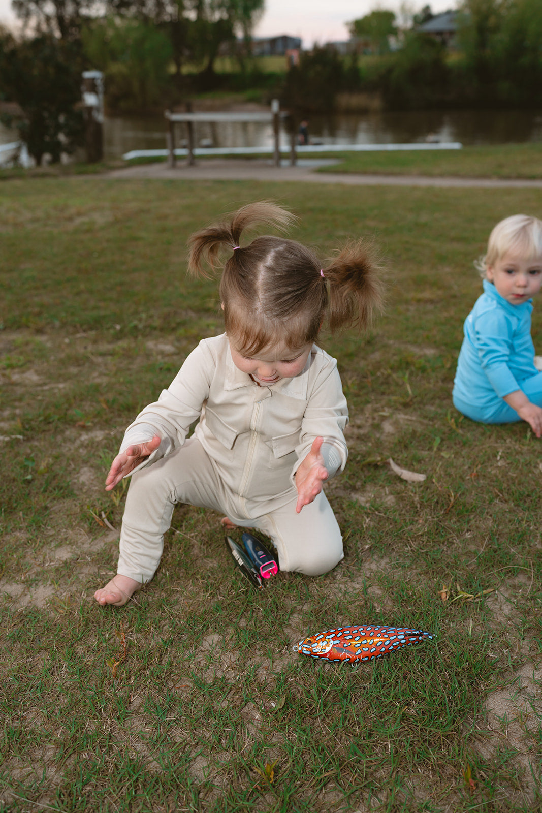 Two children playing on grass near a pond with fishing lures.