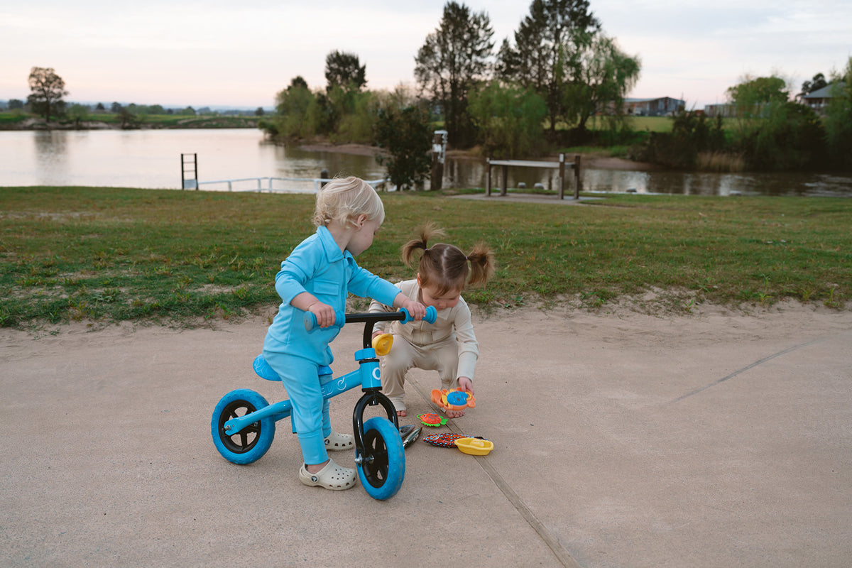 Two children playing with a balance bike by a lake.