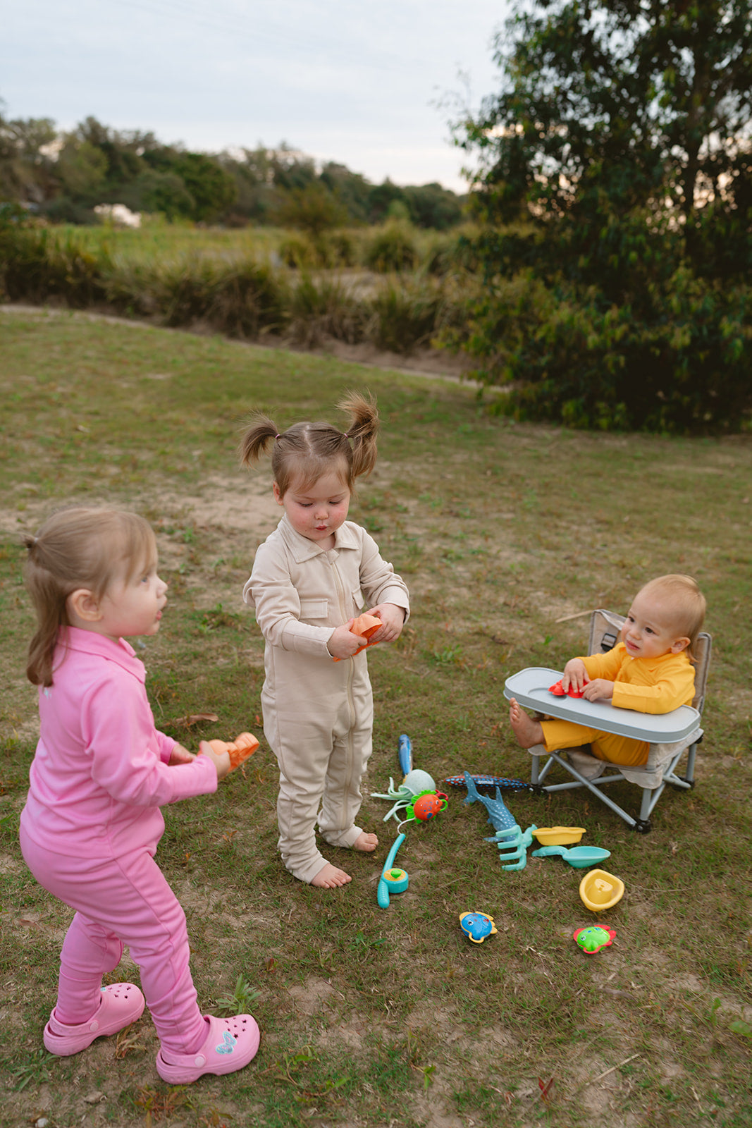 Three children playing with toys in a grassy outdoor area.